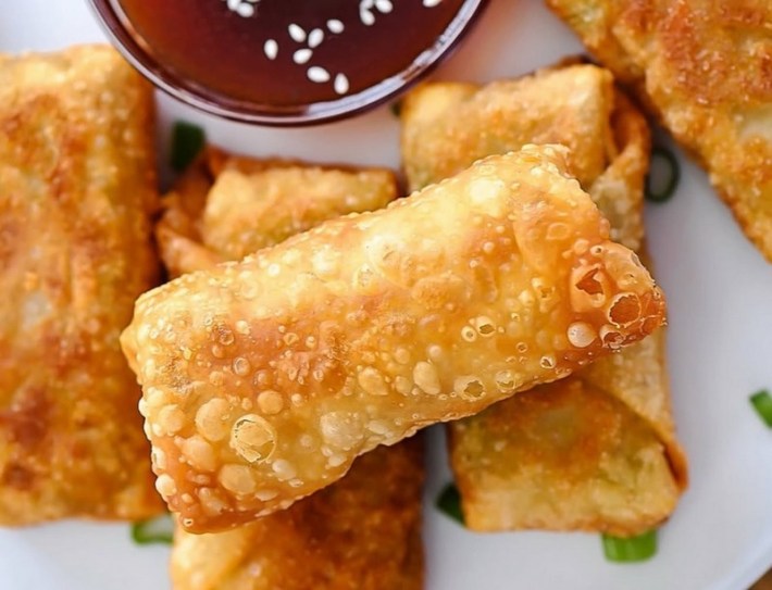 Eggrolls stacked on each other with a bowl of sauce barely showing from the top