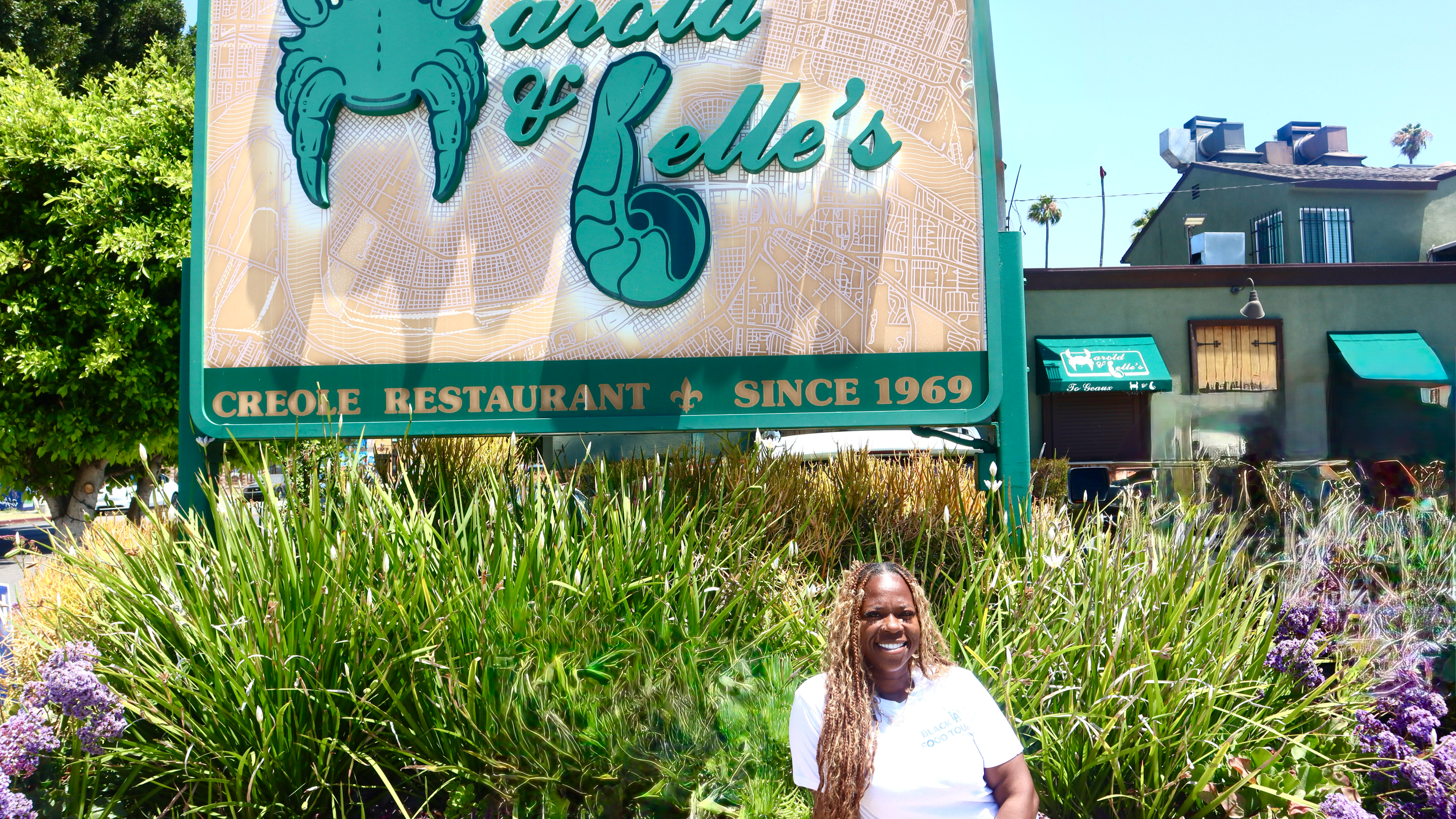 a woman in a white tee shirt smiles in front of a restaurant sign