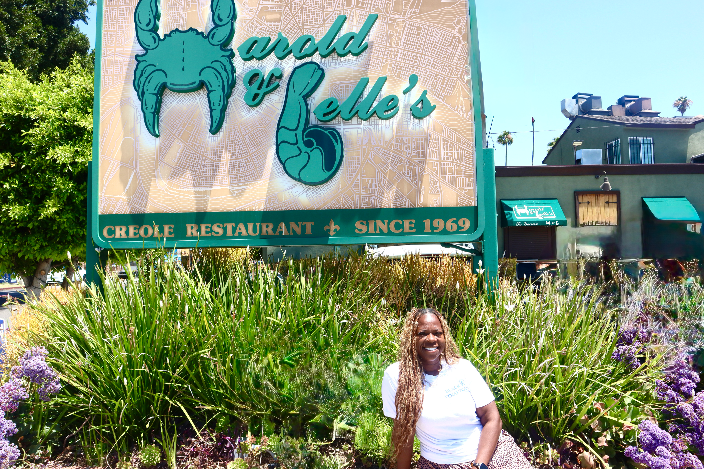 a woman in a white tee shirt smiles in front of a restaurant sign