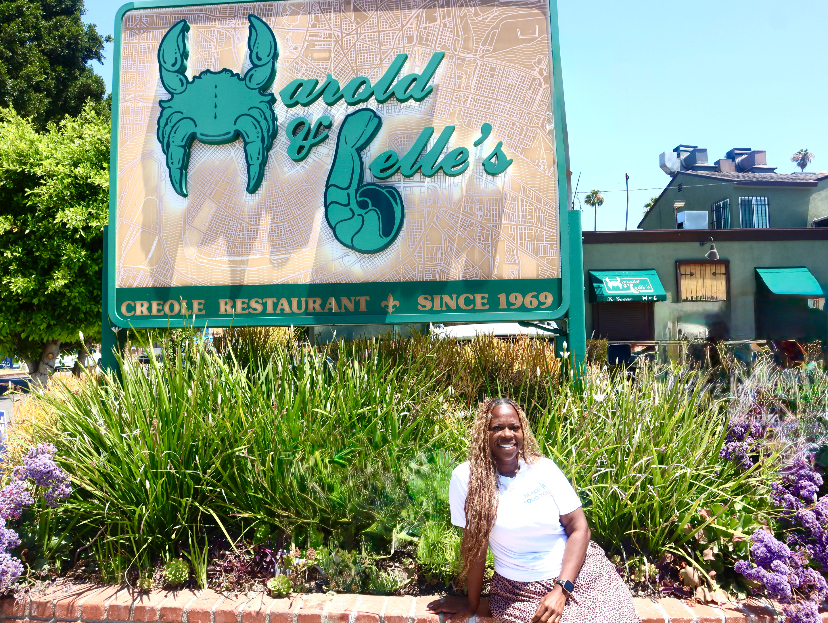 a woman in a white tee shirt smiles in front of a restaurant sign