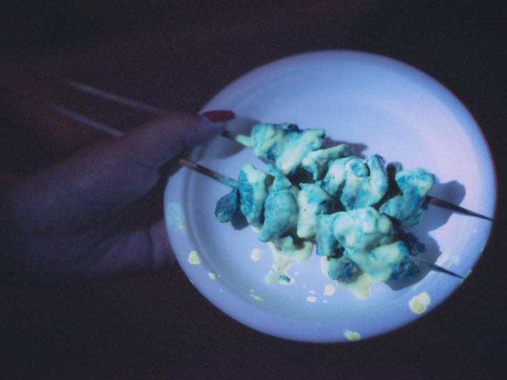 A plate of green neon chicken skewers splattered with sauce