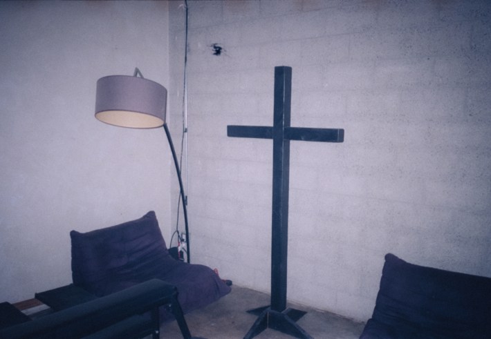 A room with a big cross, a chair, and a standing lamp