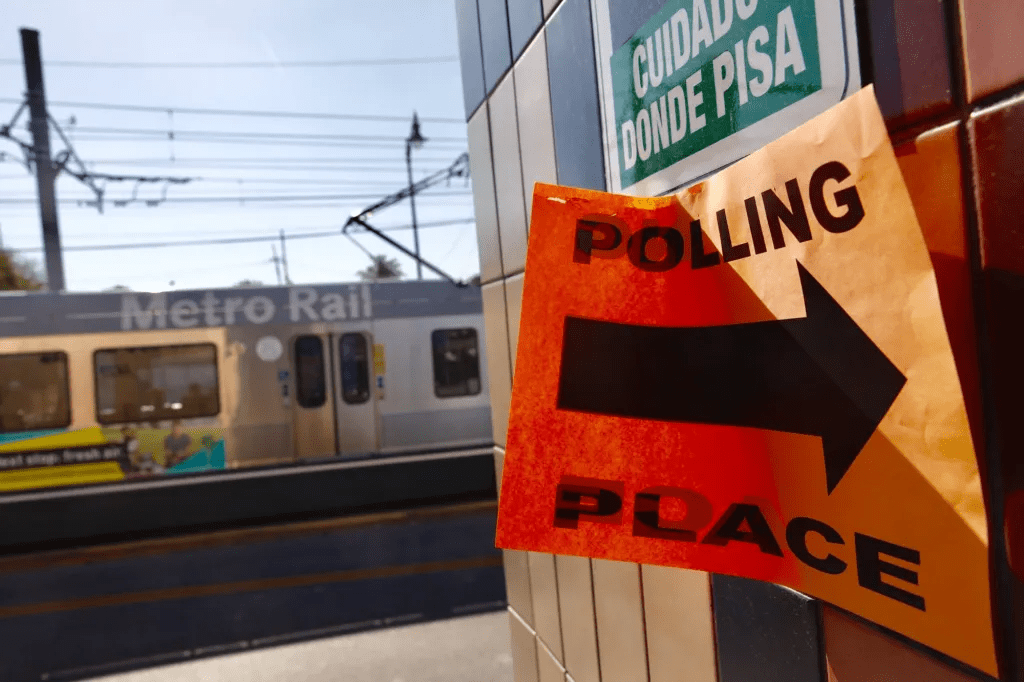 An orange sign that says Polling Place with an arrow, in front of a moving Metro train