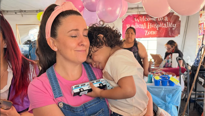 A woman known as Ms. Rachel holds a child, who puts their head on her shoulder while holding a toy truck