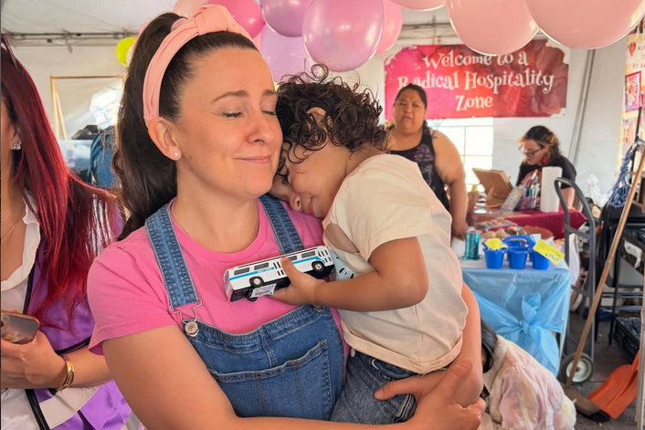 A woman known as Ms. Rachel holds a child, who puts their head on her shoulder while holding a toy truck