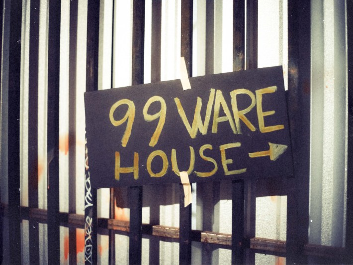 A sign that says 99 Warehouse in gold writing on a black background, hanging on a gate