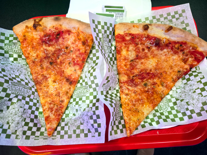 Two plain pizza slices on checkerboard green paper showing the Ninja Turtles