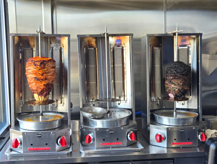 Two trompos of al pastor, one red, one black, at a restaurant