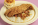 a plate of grits with vegetables, fried catfish, and a biscuit on the side