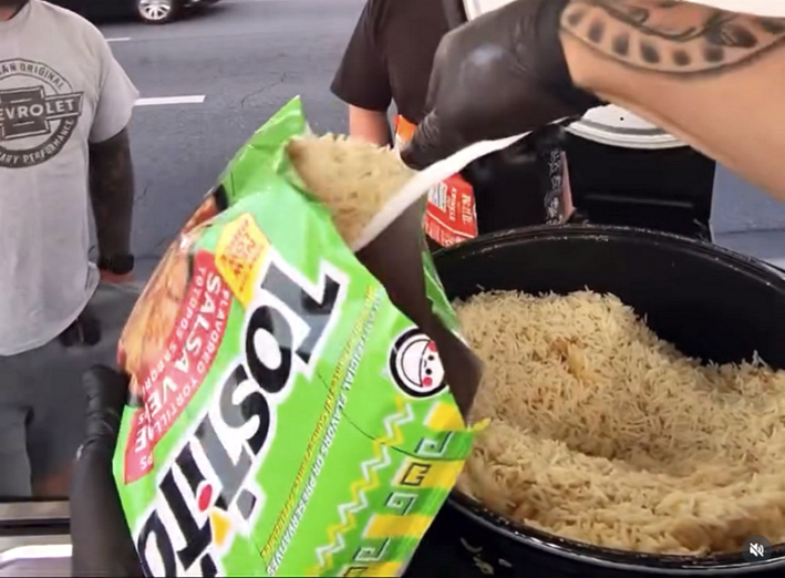 A bag of open Tostito's with rice being ladled into it at a street stand