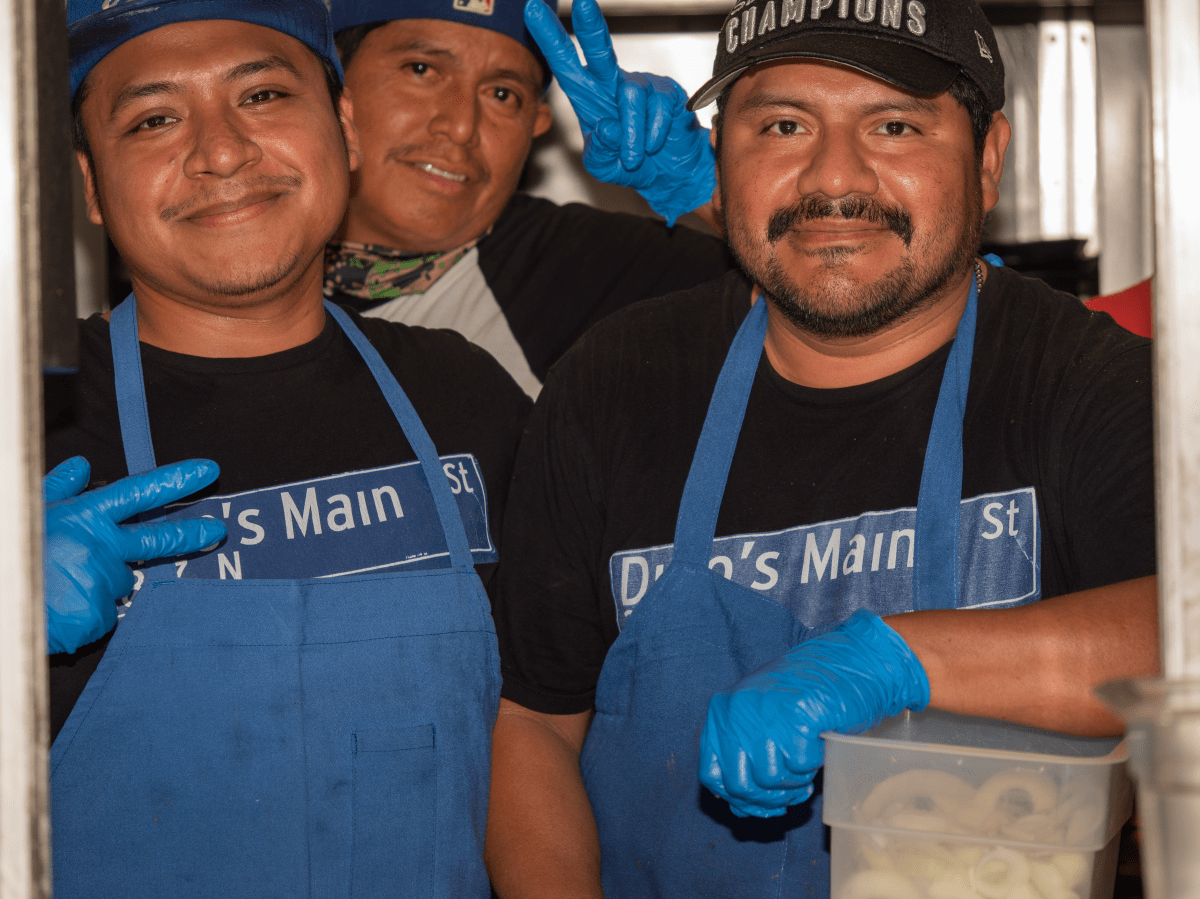 three men, two wearing blue aprons, in a restaurant