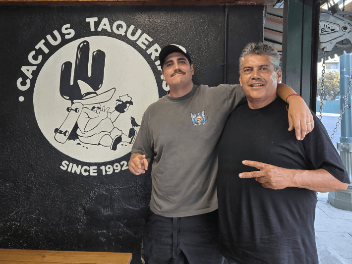 a father and son standing next to their restaurant logo