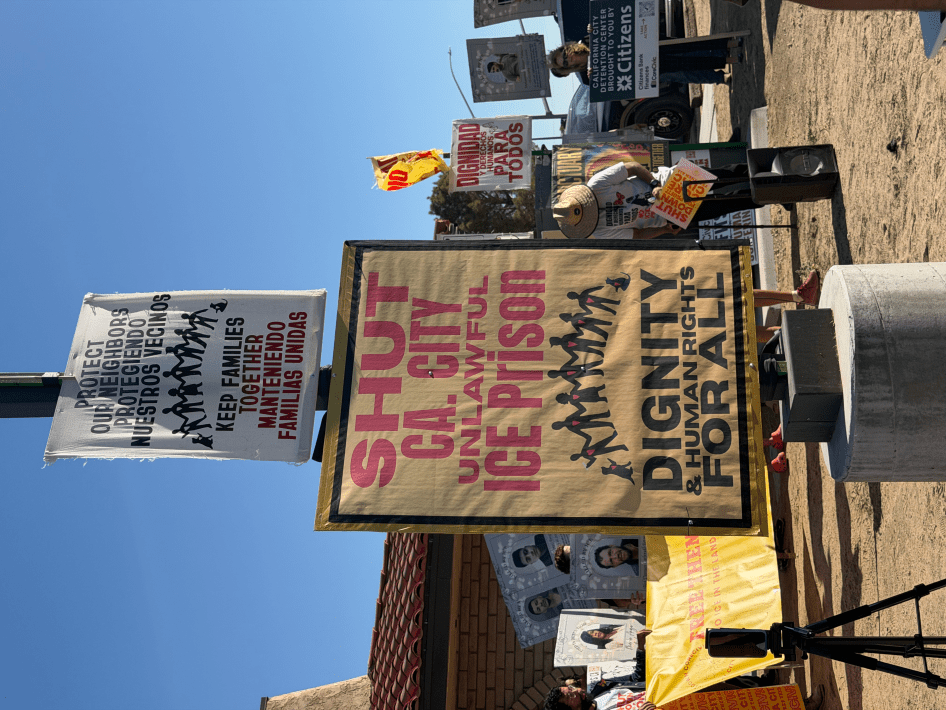 posters with messages like "SHUT CA CITY UNLAWFUL ICE PRISON. DIGNITY & HUMAN RIGHTS FOR ALL"