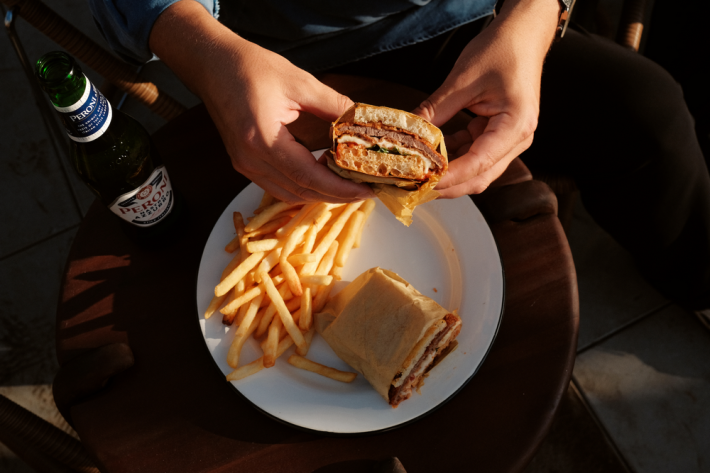 Milanesa schiacciata in someone's hands over a plate of fries and the other half fo the sandwich