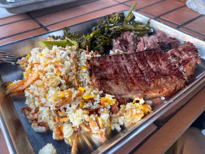 A steak with fried rice and shrimp in a metal tray