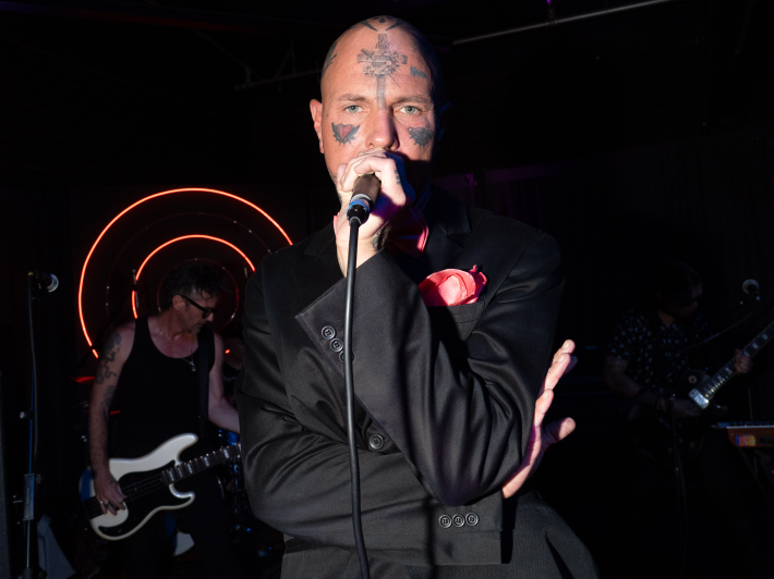 a person with face tattoos talks into a microphone