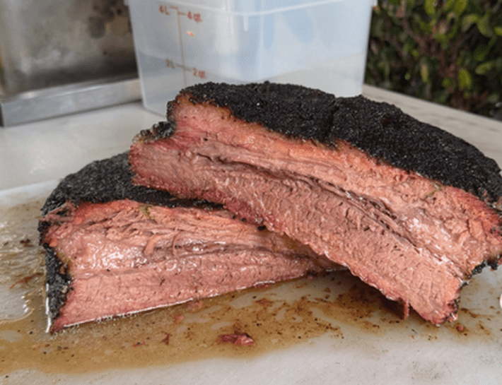 a halved brisket, with one end resting on the other and juice pooling below it