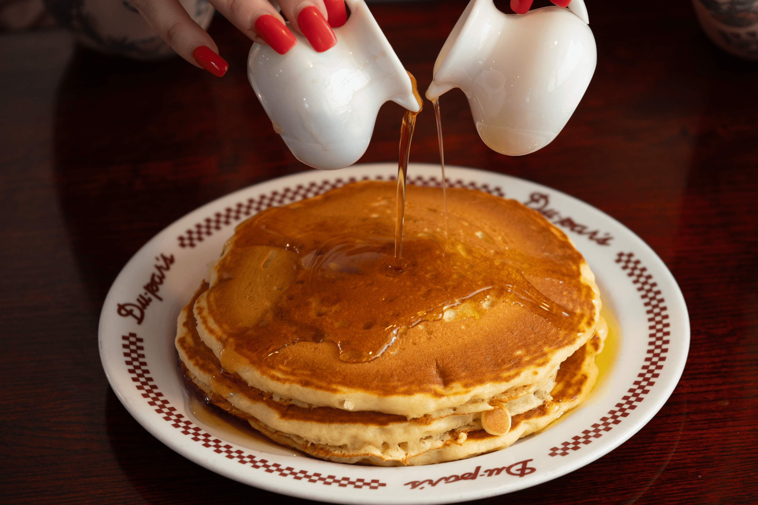 a woman pours syrup onto pancakes