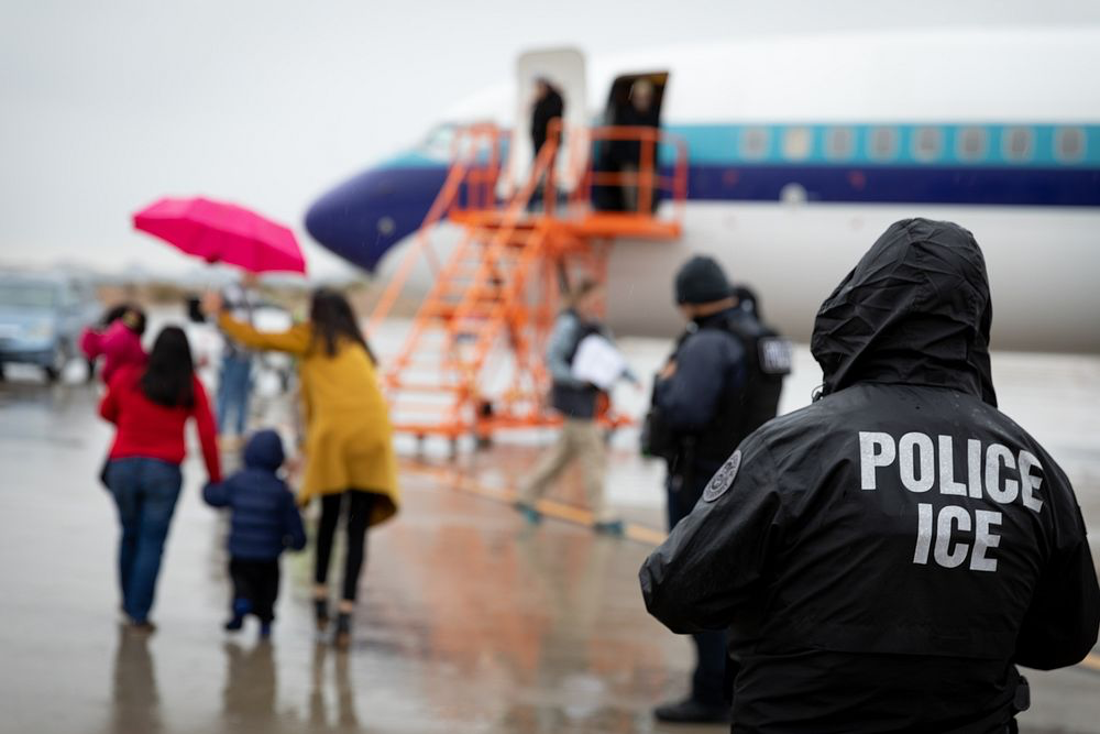 an ICE agent watches as a family boards a plane