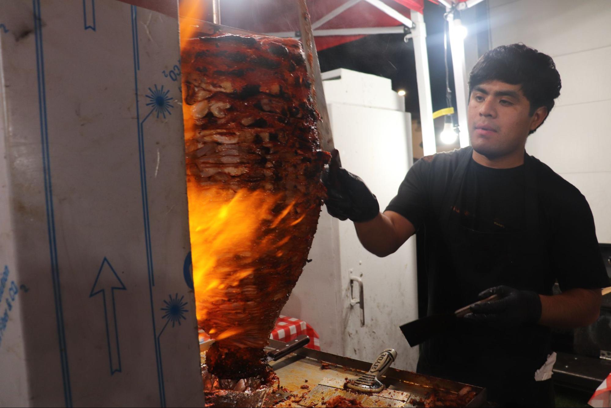 A man named Jorge cutting up the trompo at Los 3 Carnales Estilo Puebla as a blast of flame leaps out of the trompo