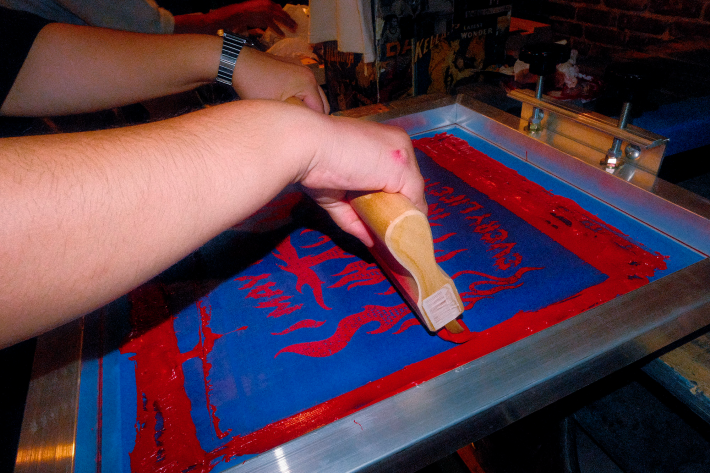 an artist drags the squeegee to spread the red ink onto the shirt