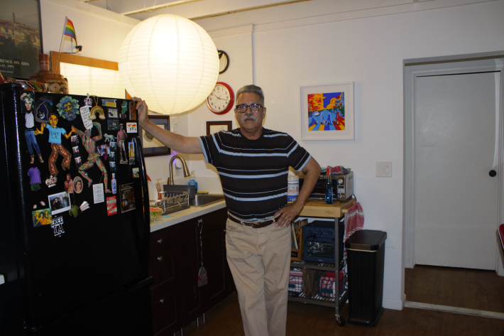 a man with a grey mustache standing with his hand on the black fridge next to him