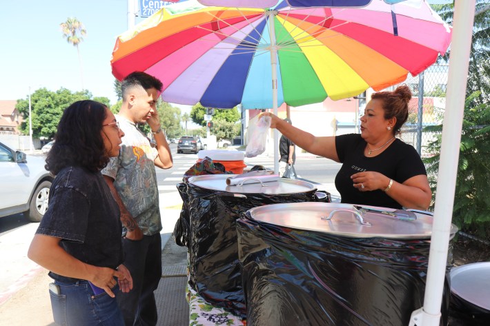 a woman selling food on the sidewalk to two customers