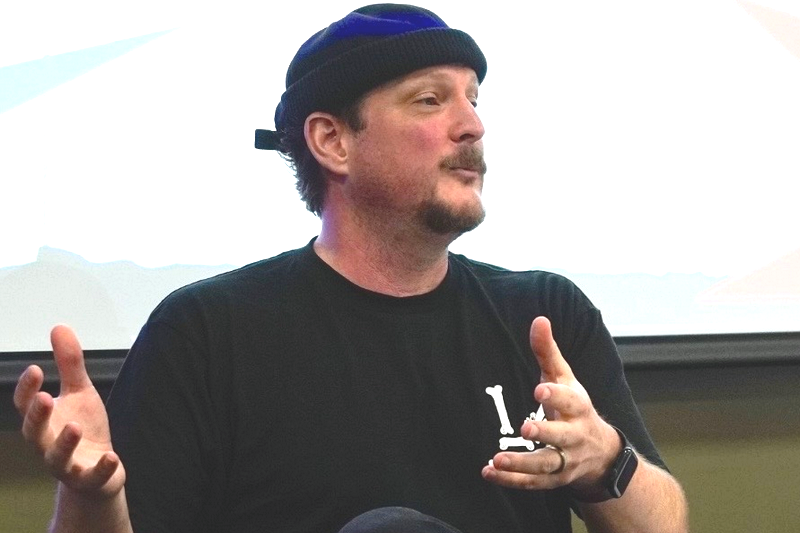 Pulitzer-nominated illustrator and cartoonist Ivan Ehlers, in a black beanie talking using his hands while seated