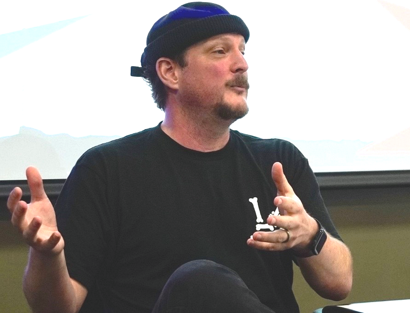 Pulitzer-nominated illustrator and cartoonist Ivan Ehlers, in a black beanie talking using his hands while seated