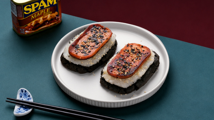 A SPAM Musubi cookie with sticky rice on black sesame mochi, next to a can of Maple SPAM