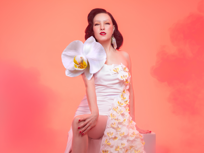 a woman poses in a dress with a large orchid on her shoulder