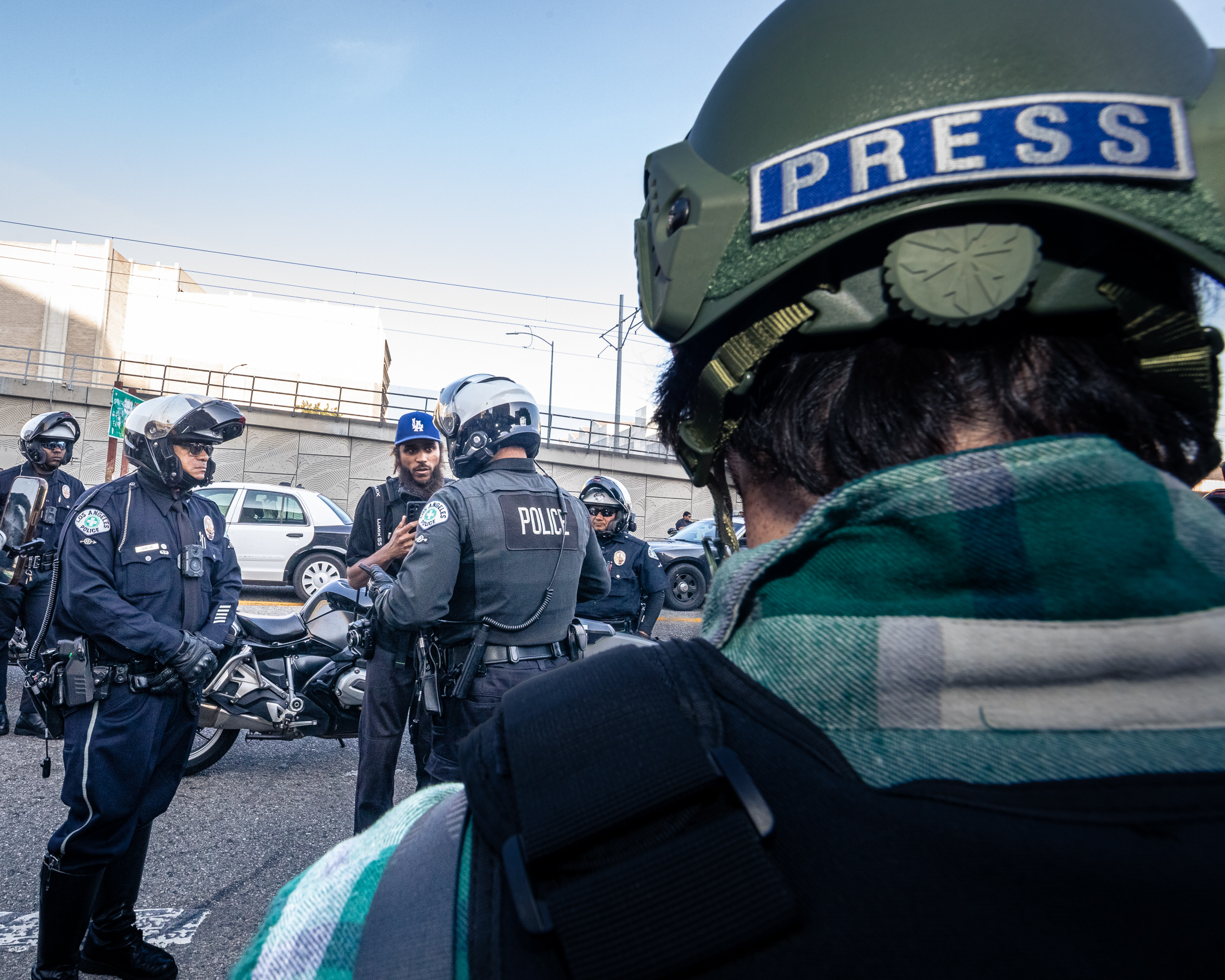 Officers surround reporter while press member wearing helmet observes.