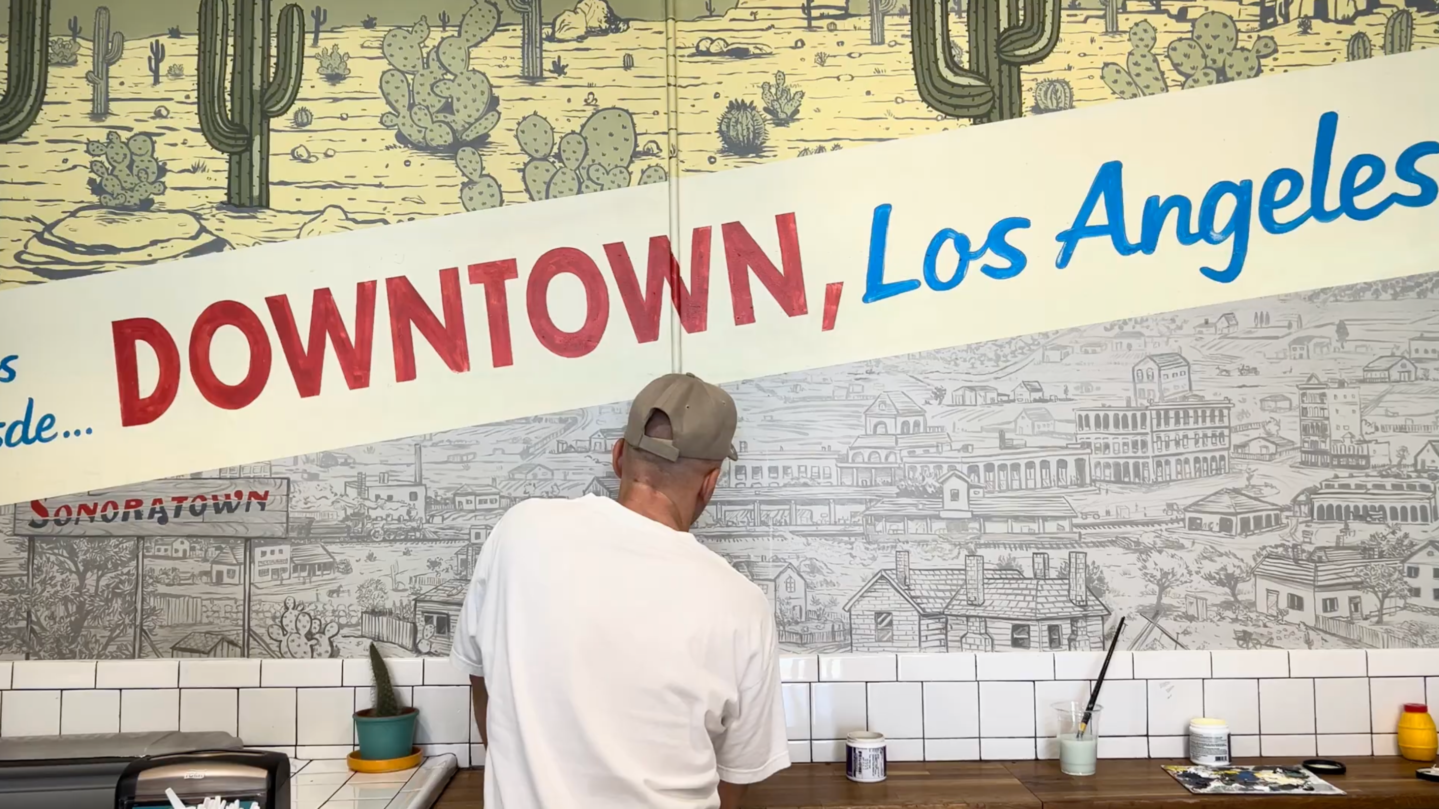 a man in a hat works on a mural