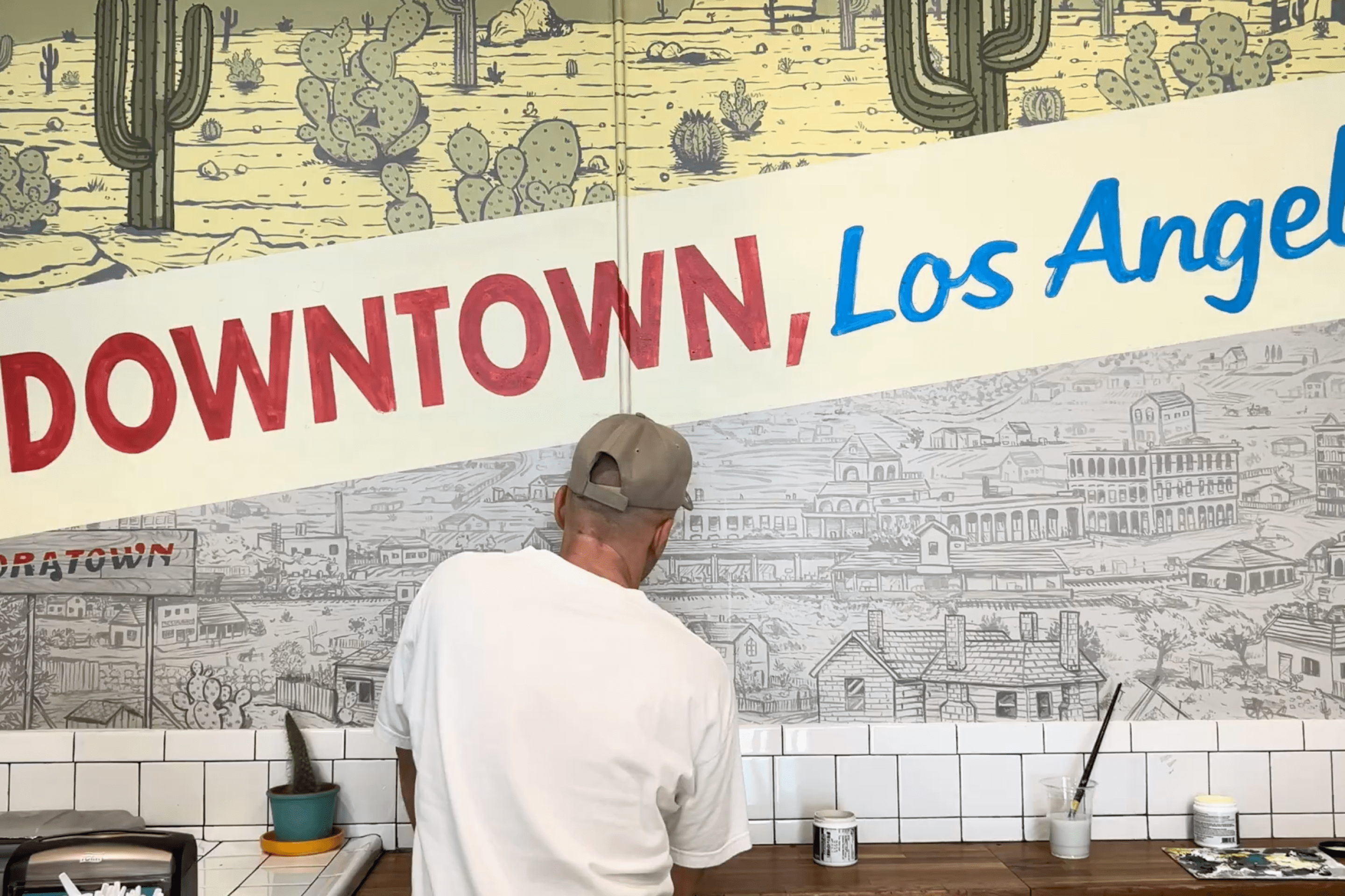 a man in a hat works on a mural