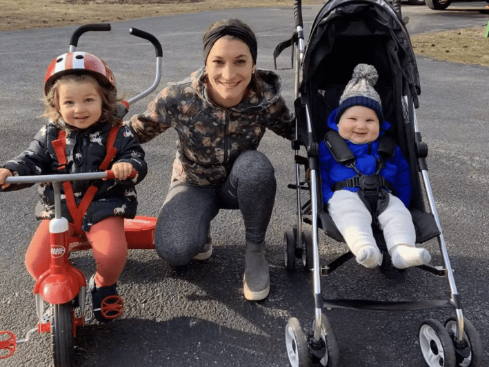 a woman and two young kids, one in a stroller and the other on a bike