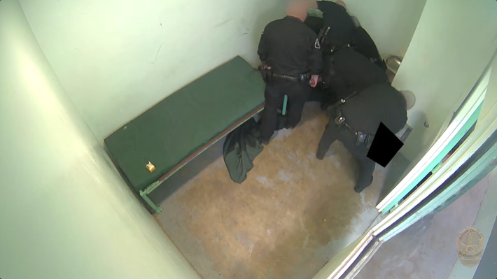 a man in jail beneath multiple officers
