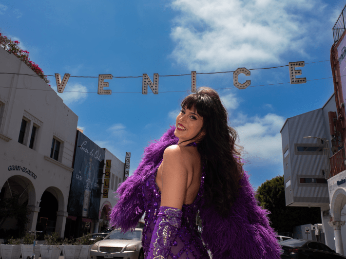 a woman with a boa posing by the Venice sign
