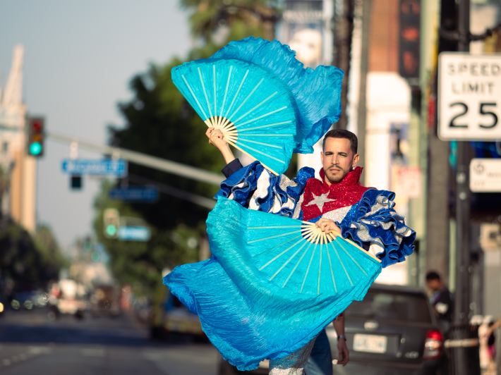 a man in a shining outfit resembling the Cuban flag performs with fans at a street intersection