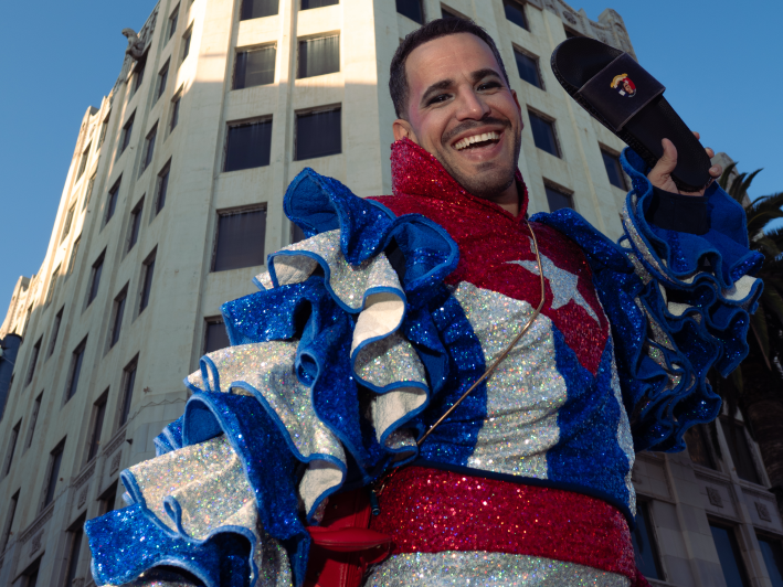 a man in a shining outfit resembling the Cuban flag holds a sandal