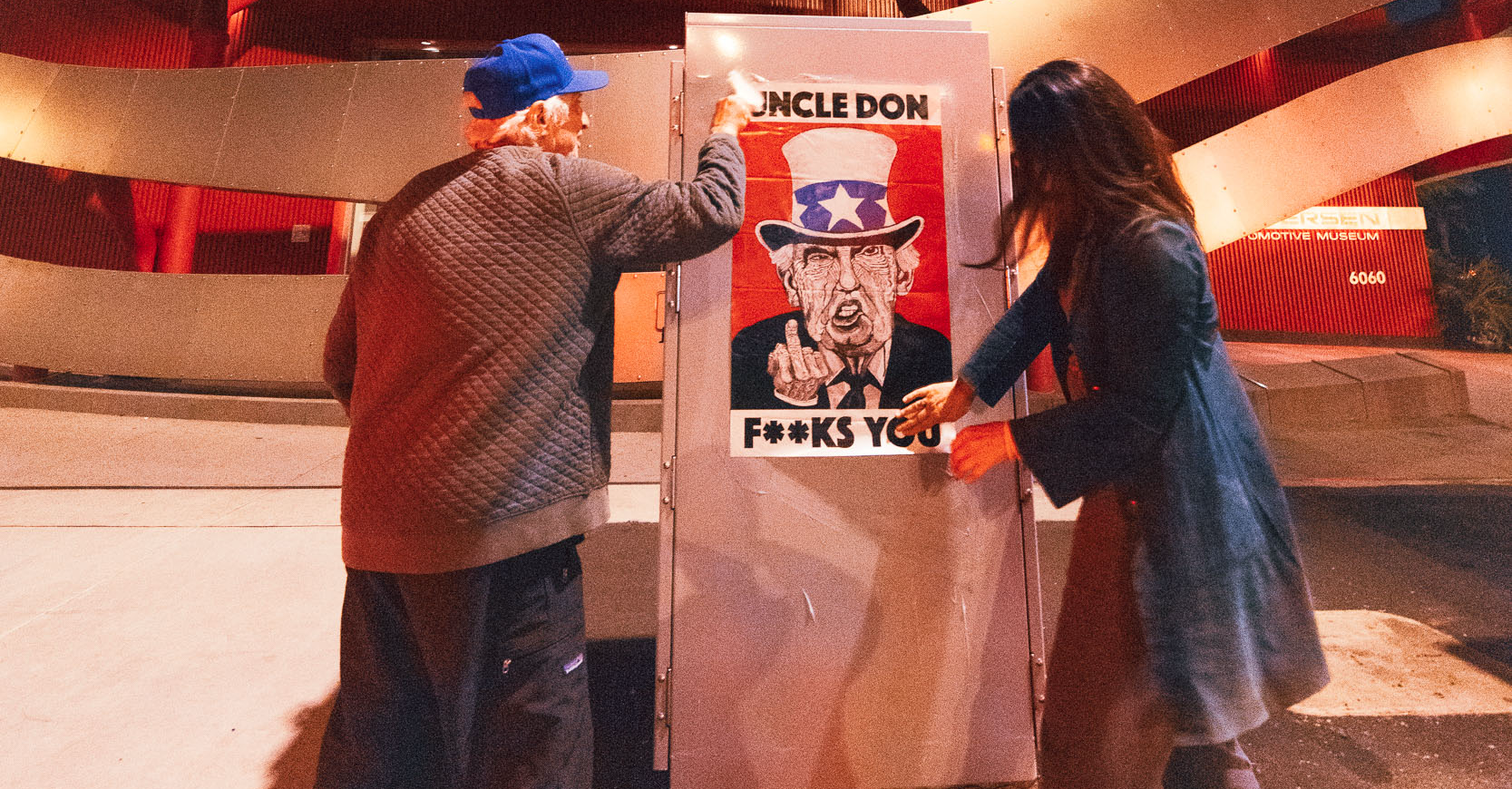 a man and woman on either side of a poster with Donald Trump's face and text that says "UNCLE DON F**KS YOU"