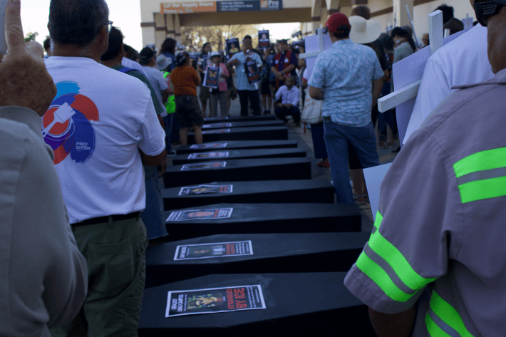 two rows of people on either side of a line of black coffins