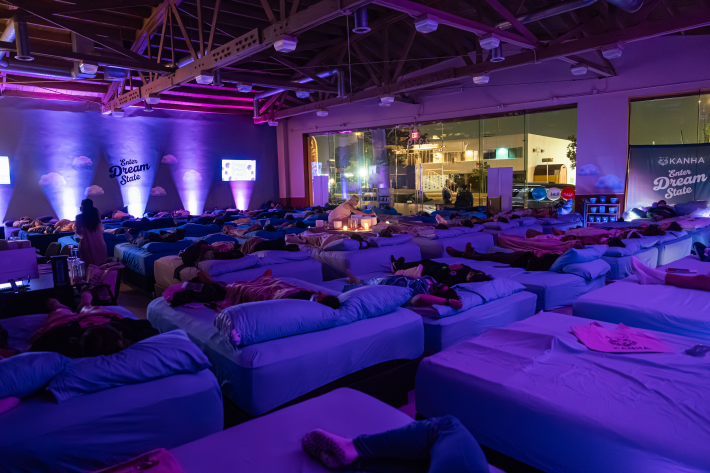 people relaxing on beds throughout a mattress store while a woman facilitates a sound bath