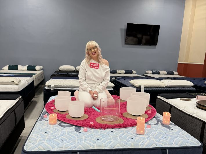 a woman sitting on a mattress surrounded with sound bowls