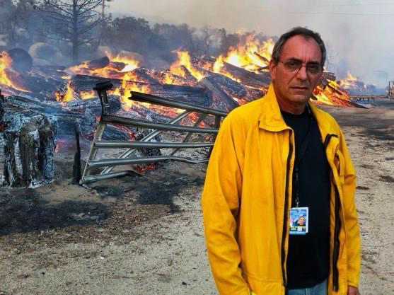 a man in a yellow jacket and glasses in front of a fire