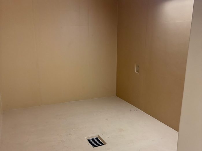 a beige, empty cell with a drain at the bottom