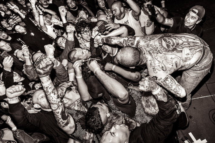 a tattooed shirtless man performs on stage for a crowd