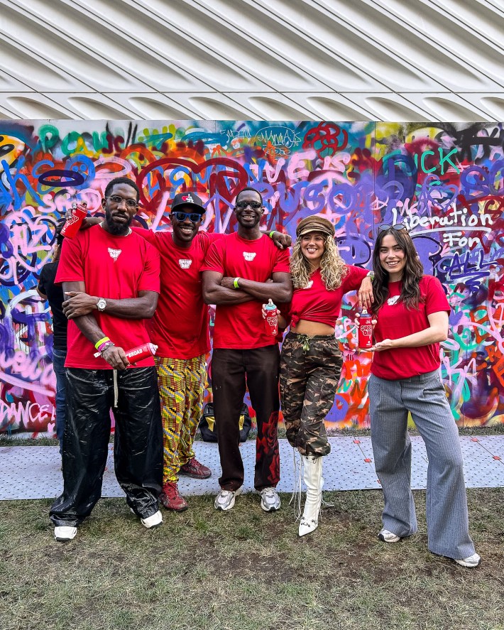 five people in red shirts smiling in front of a graffiti wall