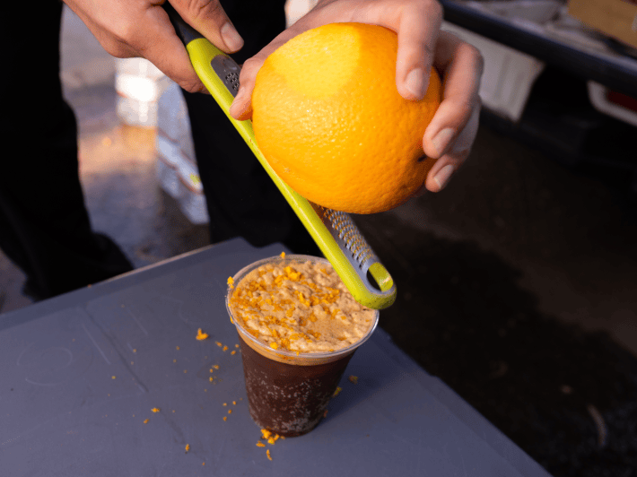 a man zests an orange above a drink