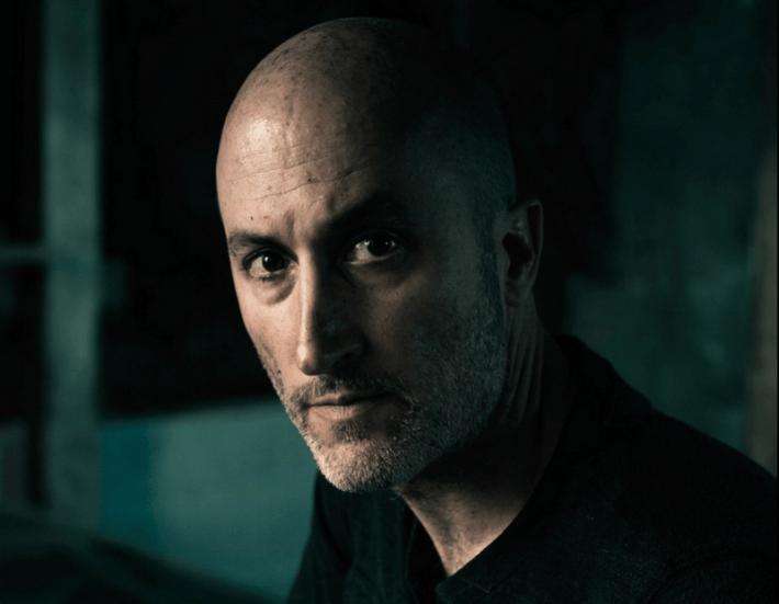 a bald man with stubble looks into the camera