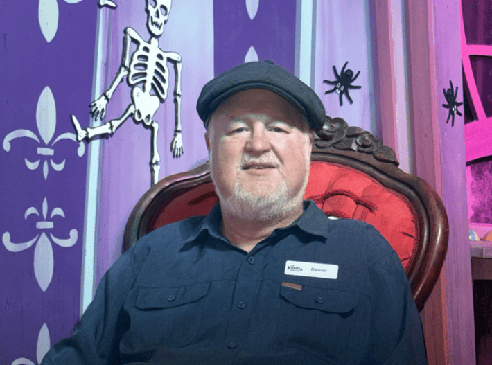 a man in a hat wearing a navy polo shirt with a nametag that says "Daniel" and Knott's Berry Farm